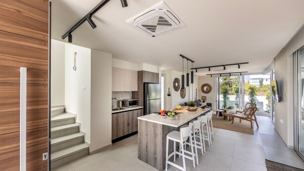A modern kitchen with a central island, a dining area with bar stools, and a staircase leading to an upper level. - Protaras Leomi Seaview Villa (Paralimni)