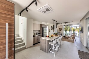 A modern kitchen with a central island, a dining area with bar stools, and a staircase leading to an upper level.