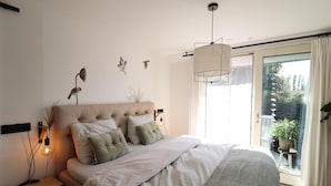 A bedroom with a large bed, a nightstand, a wall-mounted lamp, and a view of the outdoors through a sliding glass door. - Beautifully styled apartment (Betgummole)