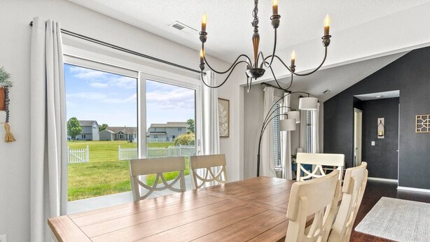 Un espace repas avec une table et des chaises en bois, un lustre et une vue sur une cour verdoyante grâce à de grandes fenêtres.