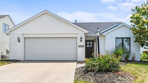 Une maison de plain-pied avec une porte de garage blanche, une porte d’entrée et un petit porche.