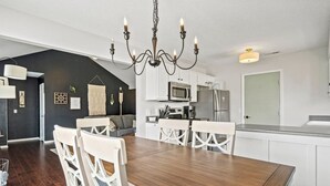 Une cuisine moderne avec des meubles blancs, une table à manger en bois et un lustre.