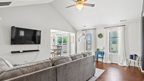 Un salon comprenant un canapé d’angle, un téléviseur à écran plat, un ventilateur de plafond et une vue sur l’extérieur grâce à de grandes fenêtres.