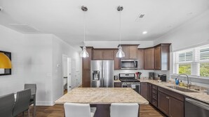 Une cuisine moderne dotée d’un îlot central, d’appareils électroménagers en acier inoxydable et de meubles de rangement en bois.
