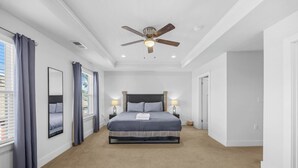 Une chambre à coucher avec un lit, deux lampes de chevet, un ventilateur de plafond et une fenêtre avec des rideaux.