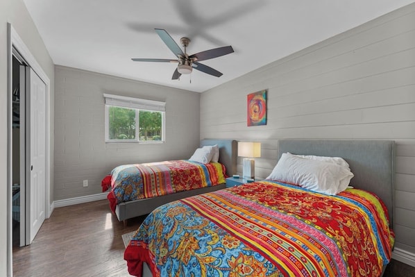 A bedroom with two beds, a ceiling fan, a window, and a door.