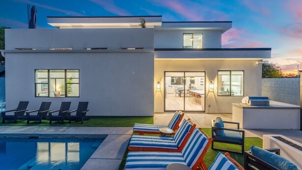 Ein modernes, zweistöckiges Haus mit Schwimmbad, Sitzgelegenheiten im Freien und einer Terrassenfläche.