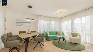 A modern living room with a green sofa, a round coffee table, and a dining area with a table and chairs. - Löning 1 - Modern vacation home with sauna, terrace & WLAN - close to the beach on Usedom (Ückeritz)