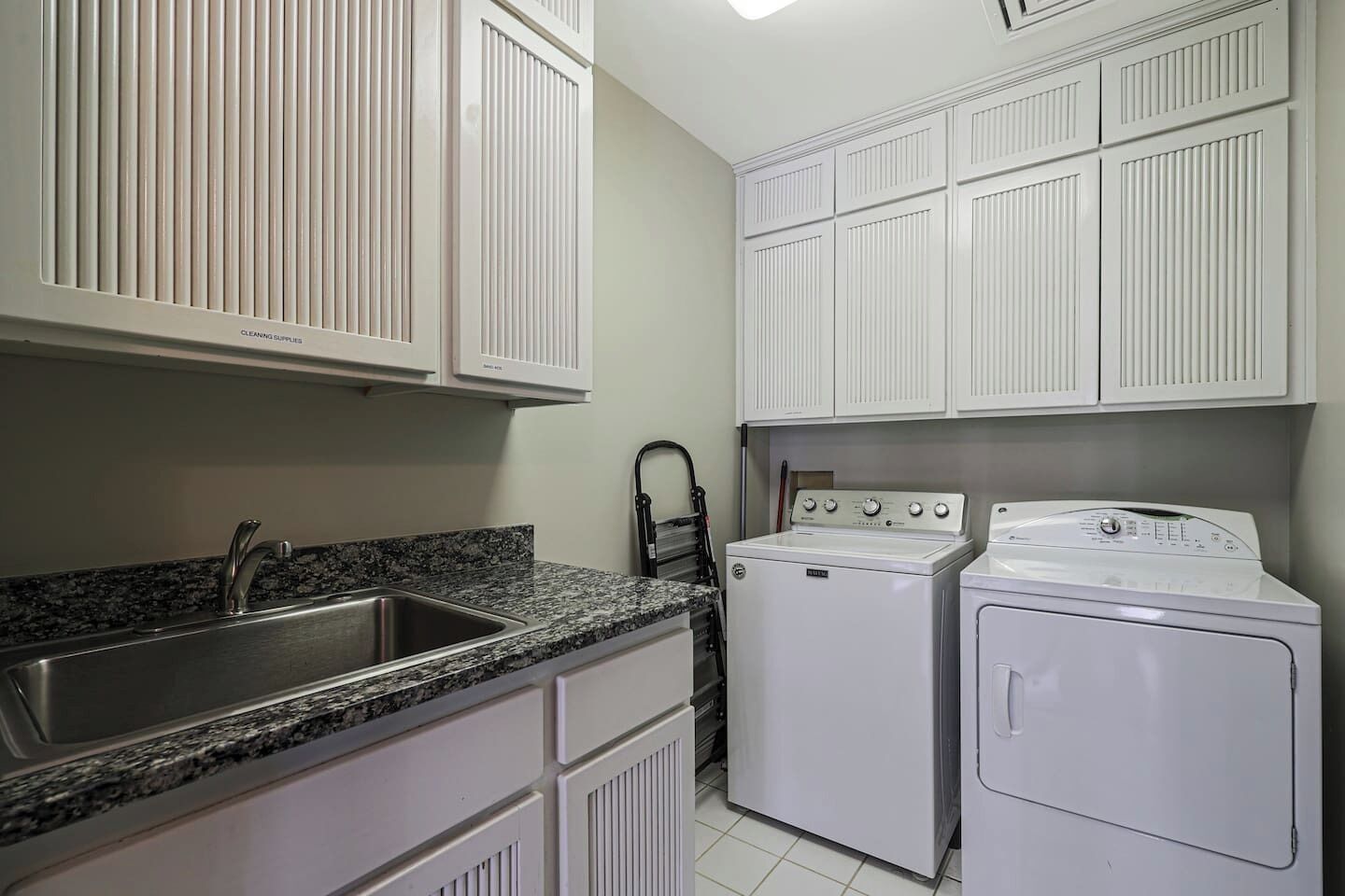 A kitchen with white cabinets, a granite countertop, a sink, a stove, and a washing machine.