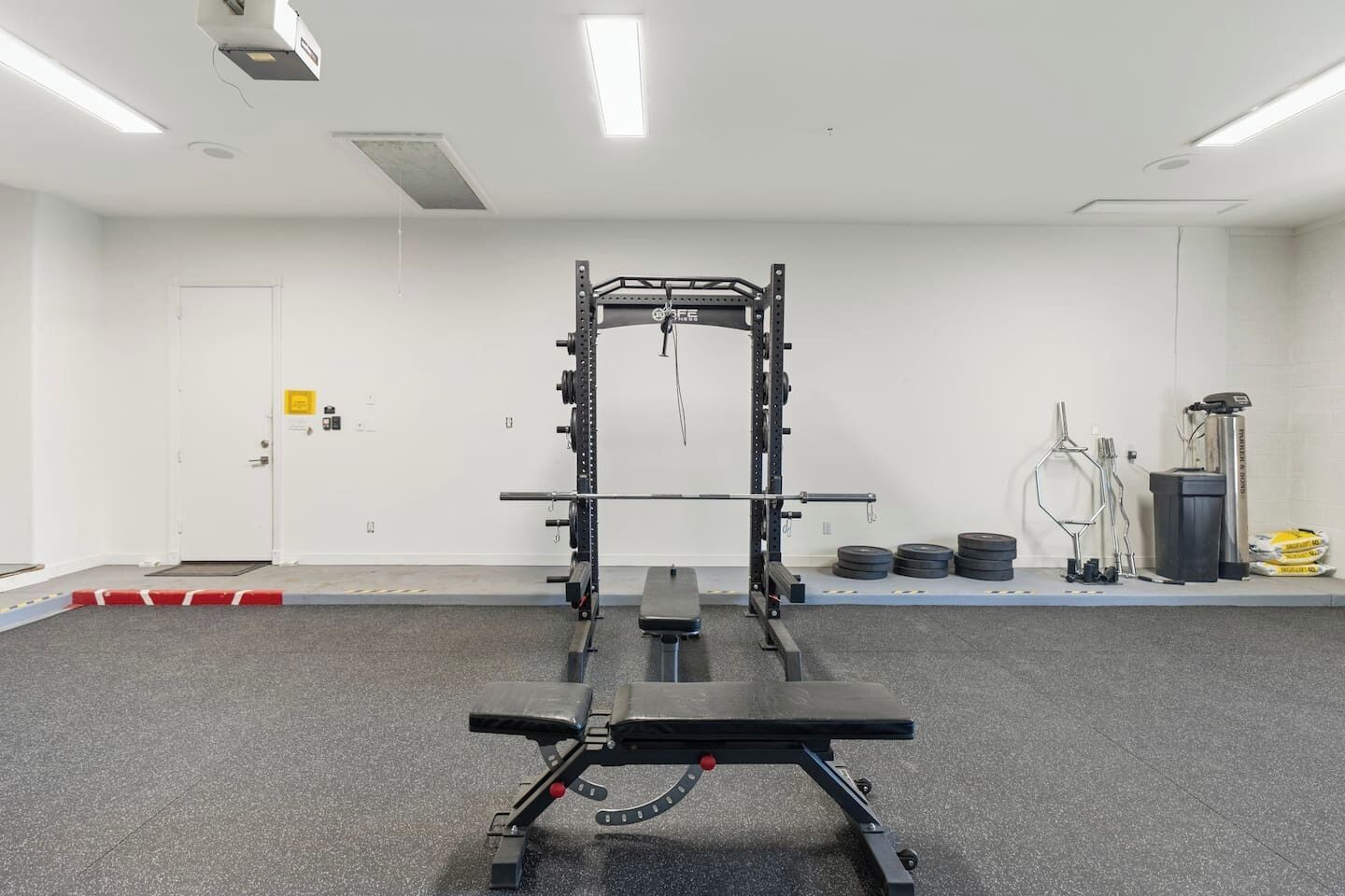 A gym with a squat rack, bench press, and weight plates.