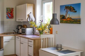 A compact kitchen with white cabinets, a microwave, a kettle, and a vase with flowers. - App. 7 Granitzblick, Seedorf - Apartment 7 "Granitzblick" in Seedorf (Sellin)