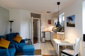 A compact living space with a kitchenette, a dining area, and a seating area with a blue sofa and a white table. - App. 7 Granitzblick, Seedorf - Apartment 7 "Granitzblick" in Seedorf (Sellin)