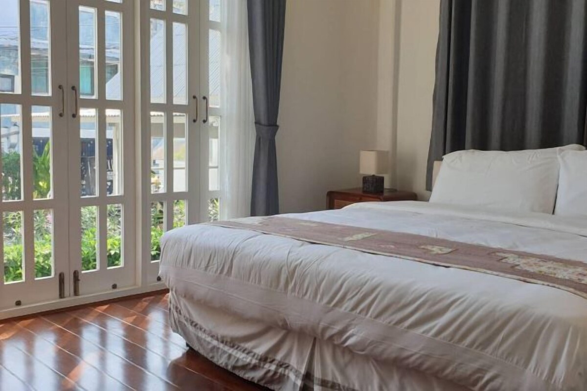 Une chambre avec un grand lit, une table de chevet avec une lampe et une vue à travers une porte vitrée.
