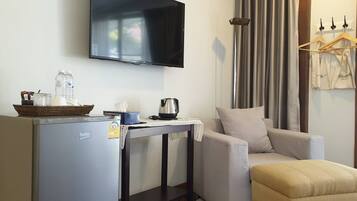 A compact living space with a kitchenette, a flat-screen TV, a sofa, and a table with a kettle and a basket.