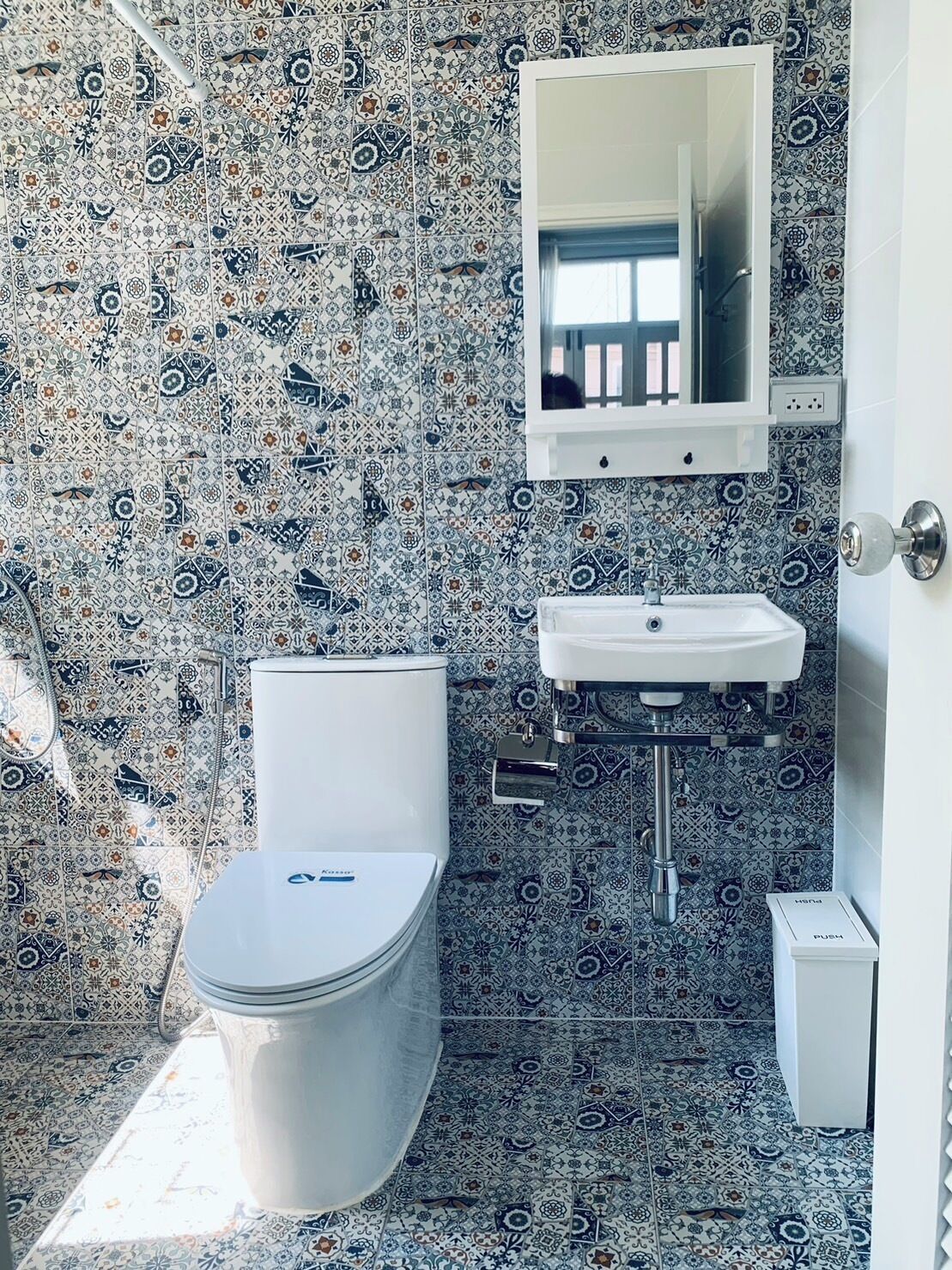 A bathroom with a toilet, sink, and mirror. The walls are tiled with a patterned design.