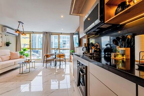 A modern apartment with a kitchen, dining area, and living room. It features a large window, a sofa, a coffee table, and a kitchen counter with appliances and utensils.