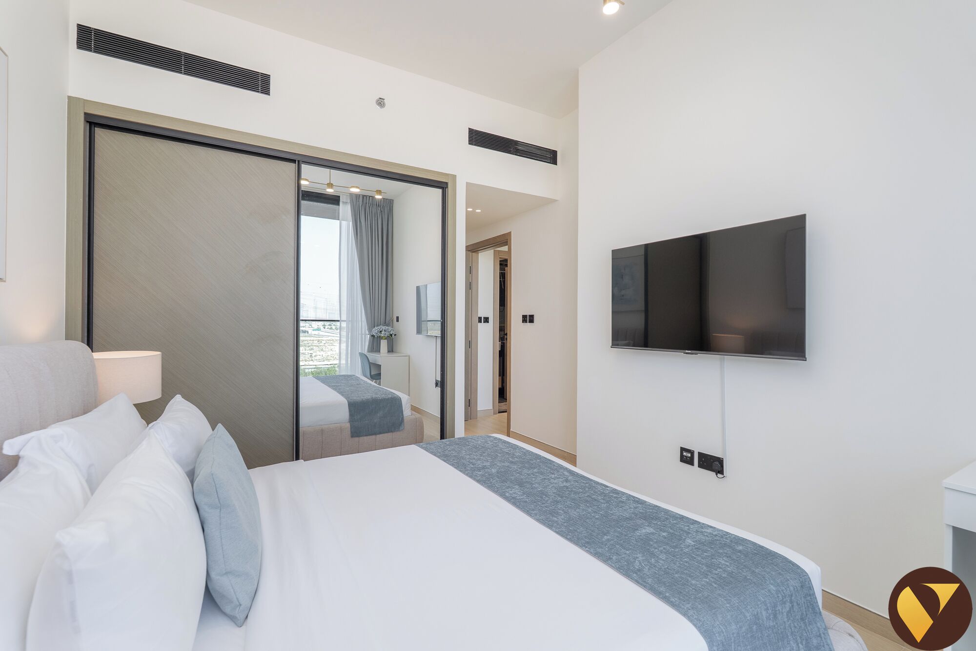 Een moderne hotelkamer met een groot bed, een aan de muur bevestigde televisie en een schuifdeur naar een balkon.