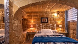 Ein Schlafzimmer mit Steinwänden, einem Bett, zwei Nachttischen und einem gerahmten Bild an der Wand.