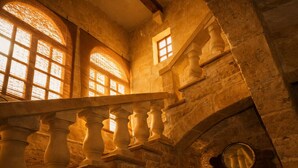 Eine Steintreppe mit Balustraden, Bogenfenstern und einem kleinen Spiegel an der Wand.
