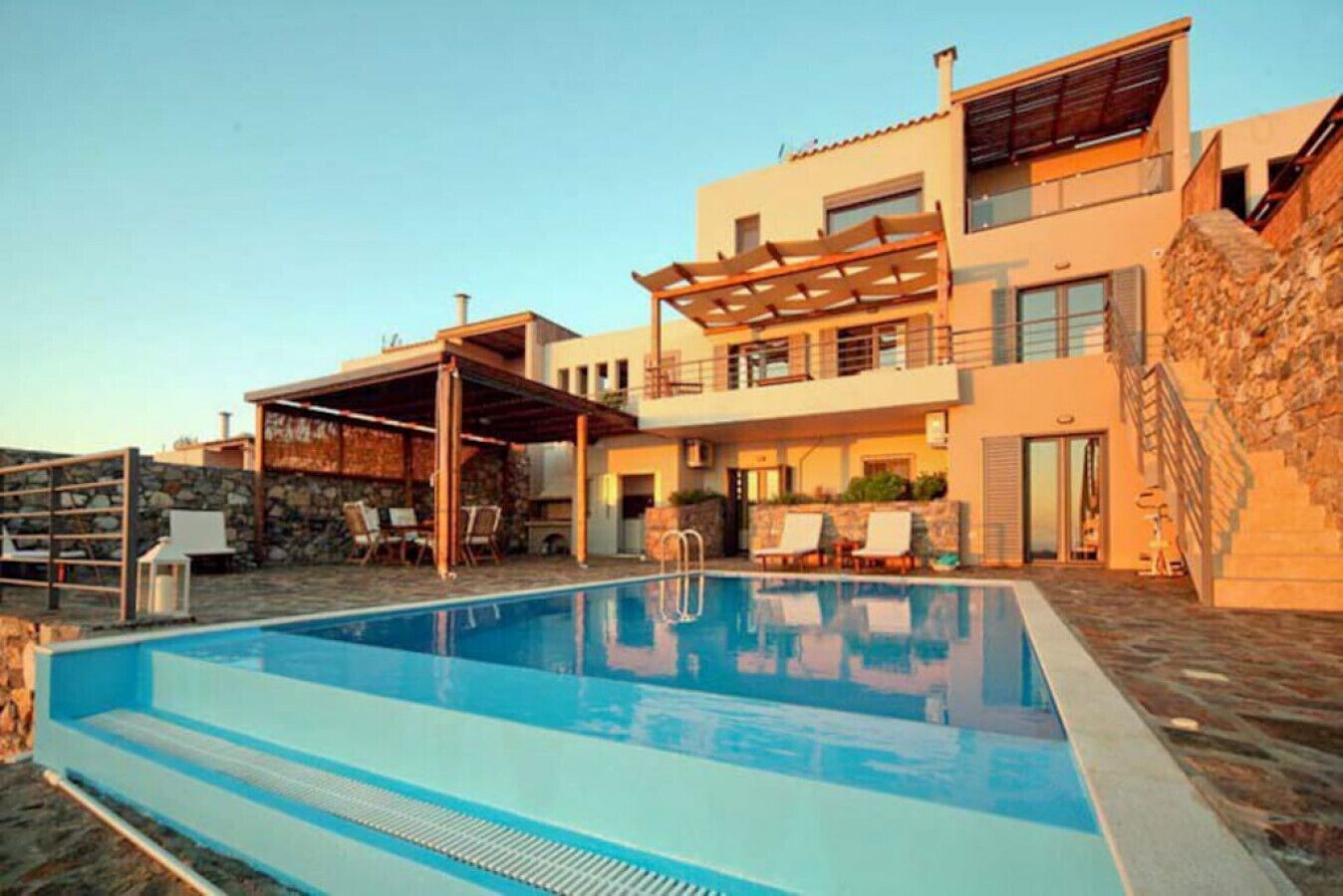 A modern two-story house with a swimming pool, outdoor seating, and a stone wall.