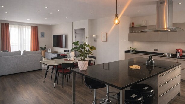 A modern kitchen with a central island, a dining area with a table and chairs, and a living room with a sofa and a TV.