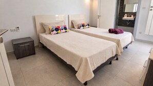 A hotel room with two beds, a small bedside table, a bathroom with a mirror and sink, and a door leading to another room. - Ensuite Twin + Laundry, Pembroke (Pembroke)