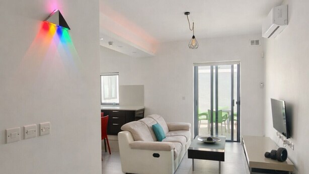 A modern living room with a sofa, a coffee table, and a TV. There is a kitchen area in the background with a dining table and chairs. - Ensuite Twin + Laundry, Pembroke (Pembroke)