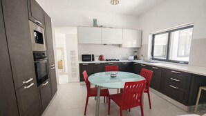A modern kitchen with dark cabinets, a glass dining table, and red chairs. - Cozy Double Room in Pembroke (Pembroke)