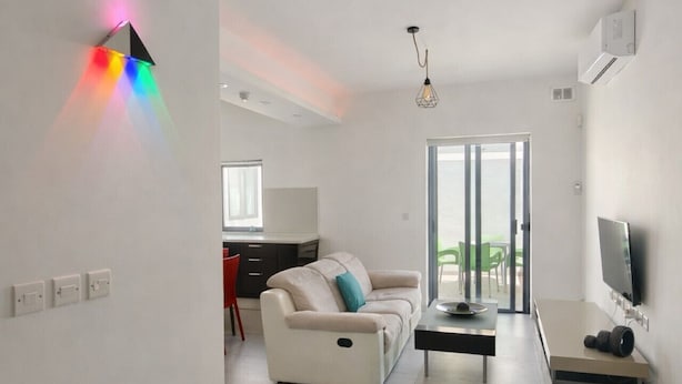 A modern living room with a sofa, a coffee table, and a TV. There is a kitchen area in the background with a dining table and chairs. - Cozy Double Room in Pembroke (Pembroke)