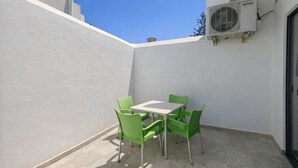 A small outdoor patio with a white table and four green chairs, an air conditioning unit mounted on the wall, and a clear blue sky in the background. - Cozy Double Room in Pembroke (Pembroke)