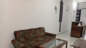 A living room with a patterned sofa, a glass-top coffee table, and a wooden side table. - BLOOM STAY  (Amritsar)