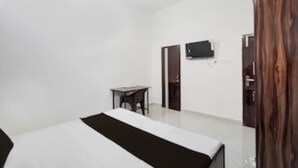 A hotel room with a bed, a small table, a TV mounted on the wall, and a wardrobe. - BLOOM STAY  (Amritsar)