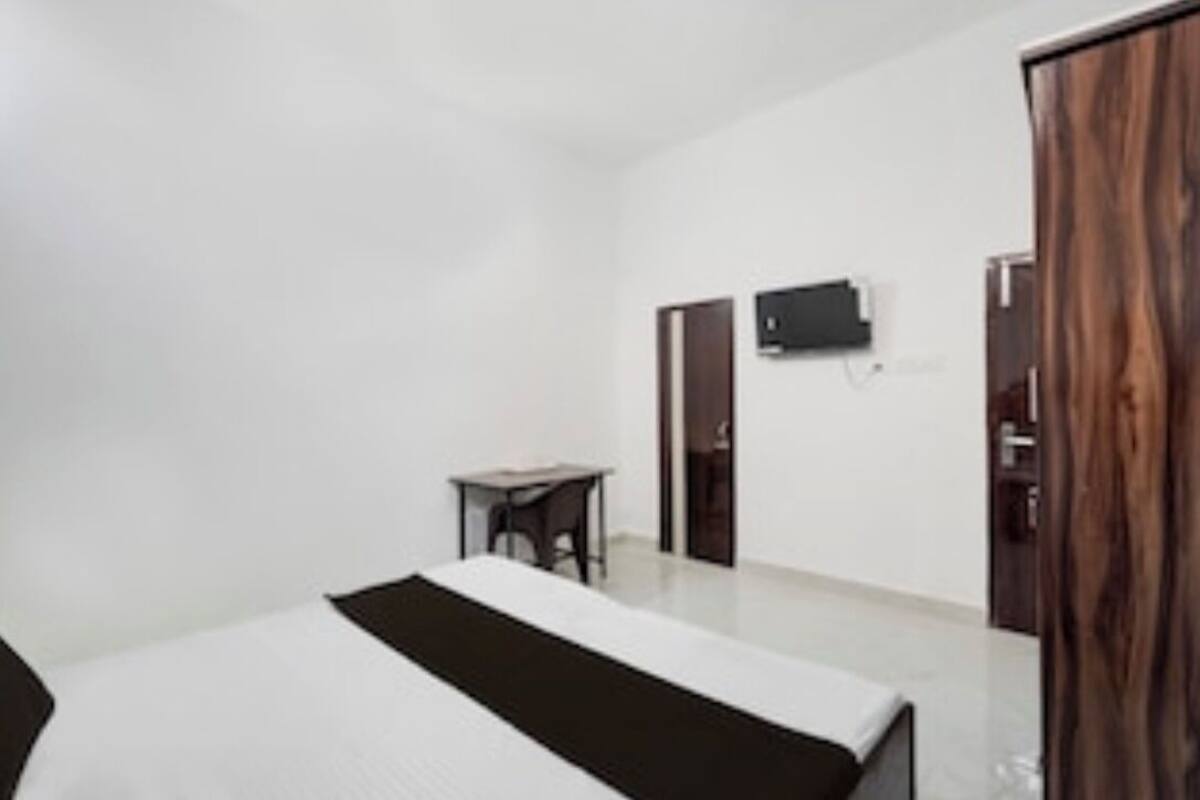 A hotel room with a bed, a small table, a TV mounted on the wall, and a wardrobe.