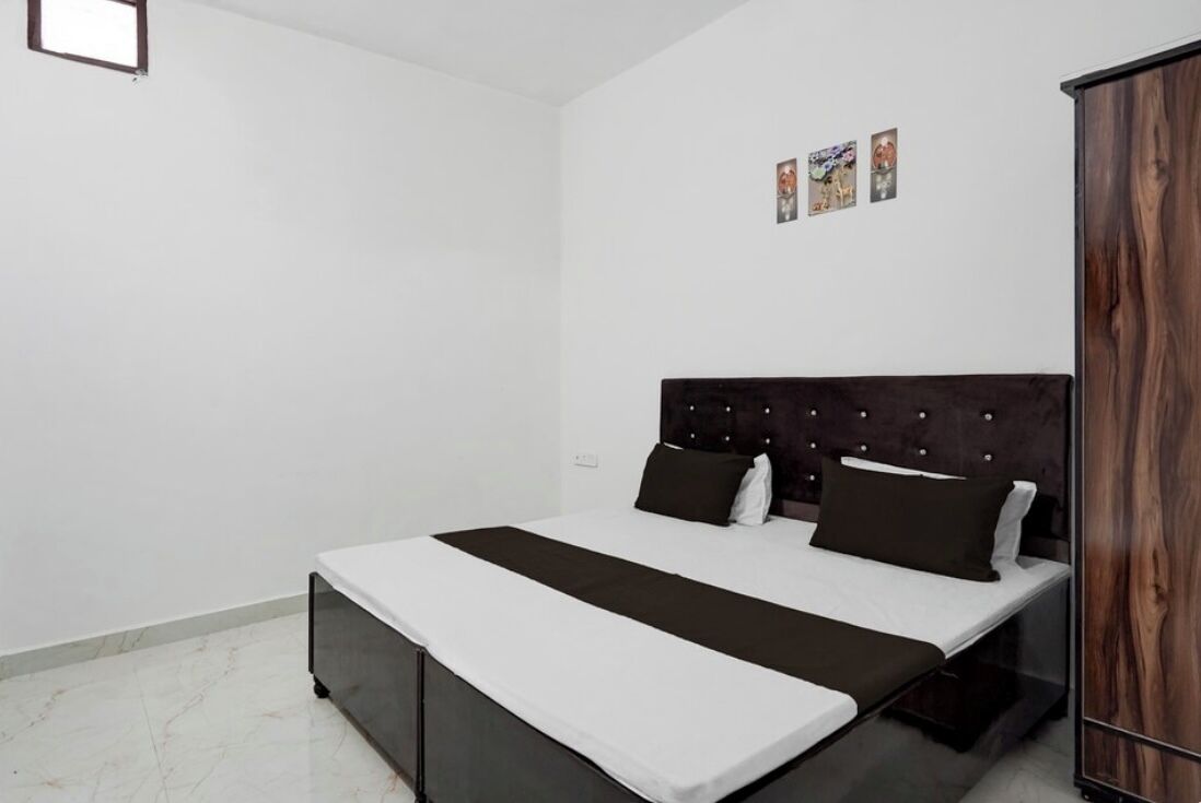 A bedroom with a bed, a wardrobe, and a small wall-mounted shelf with pictures.