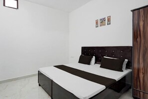 A bedroom with a bed, a wardrobe, and a small wall-mounted shelf with pictures. - BLOOM STAY  (Amritsar)