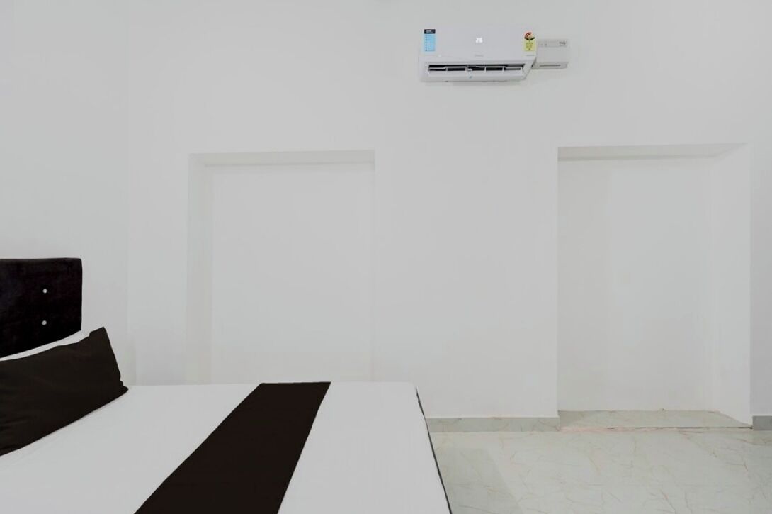 Una camera d'albergo minimalista con un letto, una parete bianca e un condizionatore d'aria.