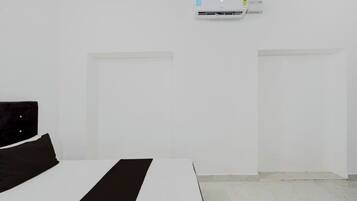 Una camera d'albergo minimalista con un letto, una parete bianca e un condizionatore d'aria.