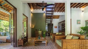 Un vaste espace de vie aménagé avec des meubles en osier, une table basse et un escalier menant à un niveau supérieur.