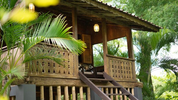 Une maison en bois dotée d’un balcon, entourée d’une végétation luxuriante.