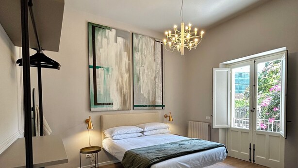 Ein Schlafzimmer mit Bett, einer Kandelaber, einem Fenster mit Aussicht und Kunstwerken an der Wand.