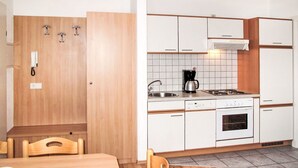 Ett kompakt kök med vita skåp, en spis, ett handfat och en kaffebryggare.