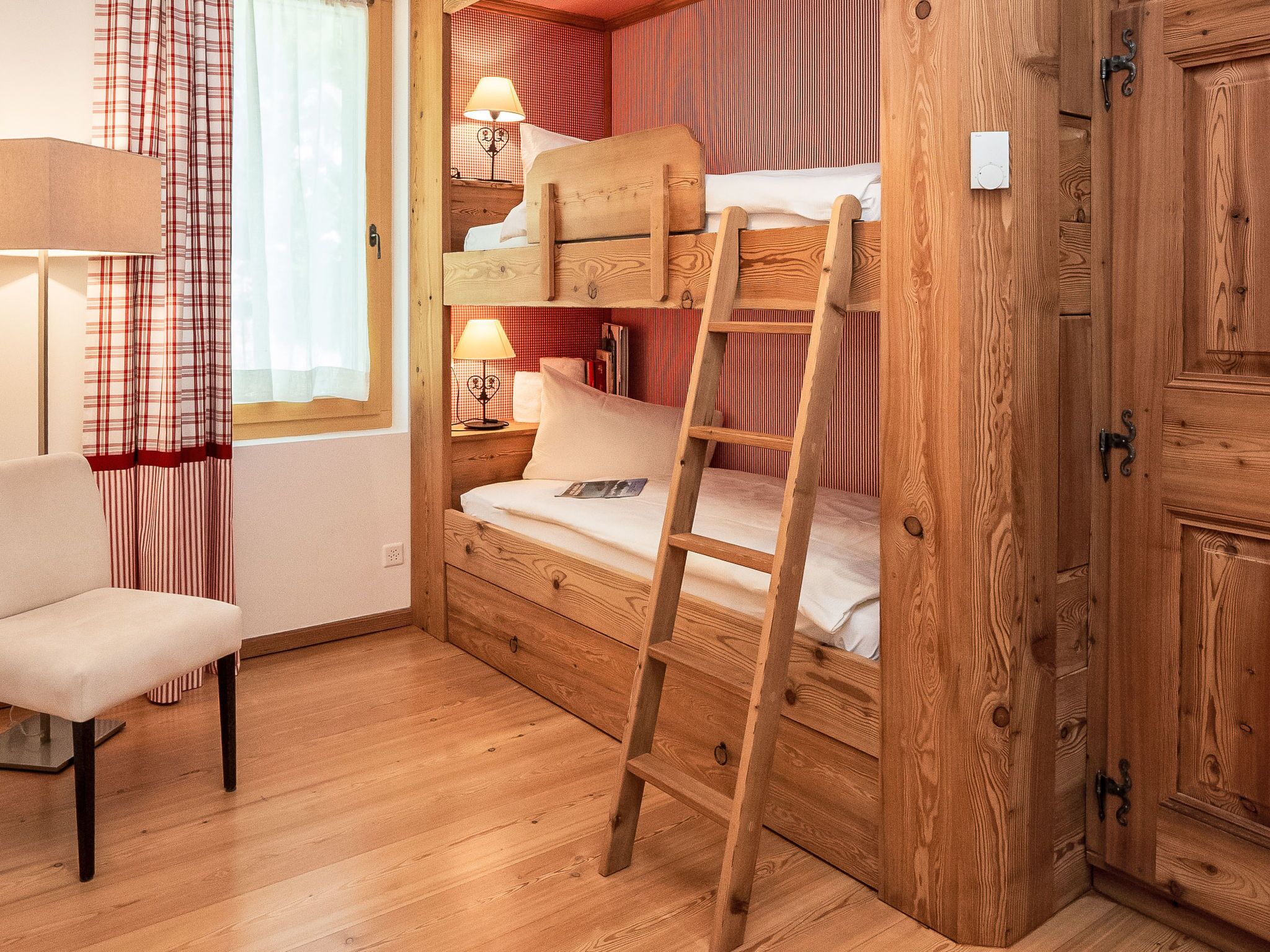 Una habitación acogedora con una cama litera, una escalera, una mesita de noche con lámpara y una silla.