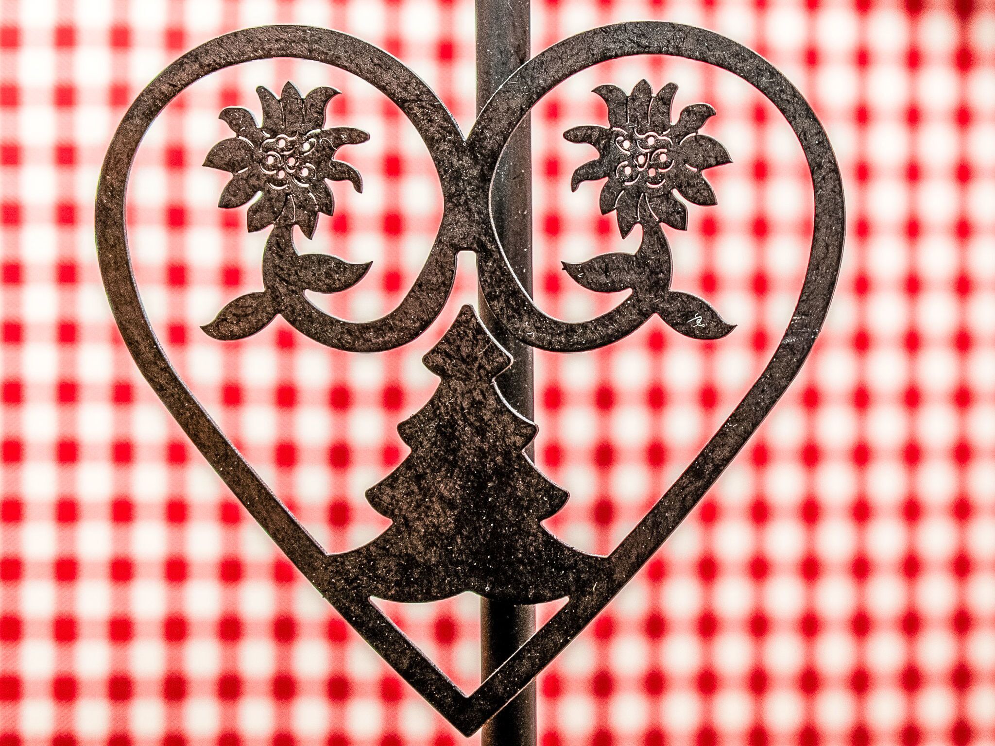 A heart-shaped metal gate with floral designs, set against a red and white checkered background.