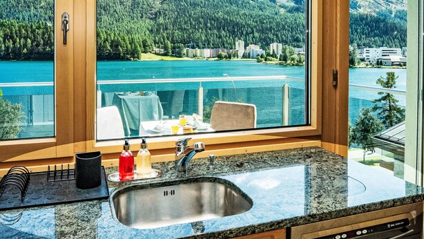 Cozinha com uma janela ampla com vista para um lago e montanhas.