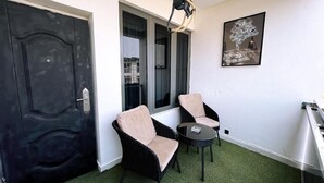 Une pièce avec deux chaises, une petite table, une porte noire et un tableau accroché au mur.