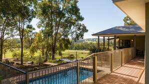 A pool area with a view of a green landscape and trees, a covered patio, and a fenced pool. - Valley View – Ferguson Valley (Ferguson)