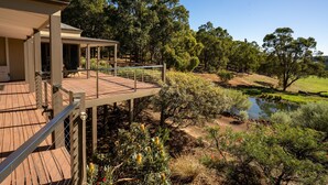 A wooden deck with a railing overlooking a landscaped garden with a pond and trees. - Valley View – Ferguson Valley (Ferguson)
