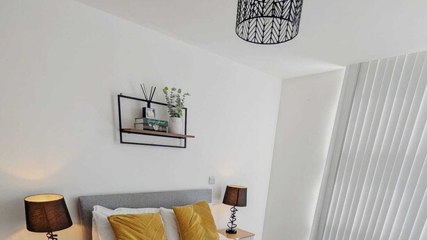 Habitación de hotel con cama, mesitas de noche, lámpara, estante con objetos decorativos y ventana con persianas.