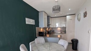 A modern kitchen with white cabinets, a marble dining table, and grey upholstered chairs.