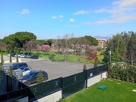 Un estacionamiento de hotel con varios coches, una valla verde y árboles con flores rosadas.